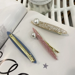 Close-up of three pearl-decorated hair clips in grey-blue, pink, and cream acetate textures