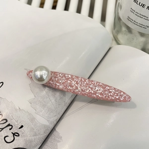 Elegant pink resin hair clip with marble texture and a large pearl on a magazine