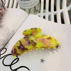Close-up of marble pattern acetate hair claw clip with yellow teeth on a white magazine