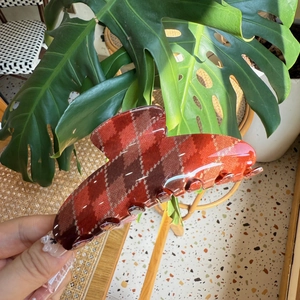 Close-up of a large red argyle pattern hair claw clip held in hand for size display