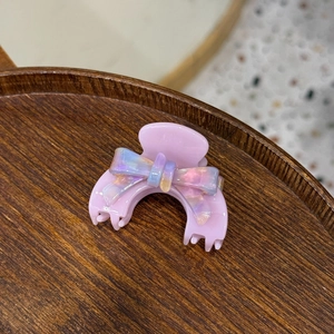 Sweet purple acetate hair claw clip with iridescent bow decoration on wooden tray