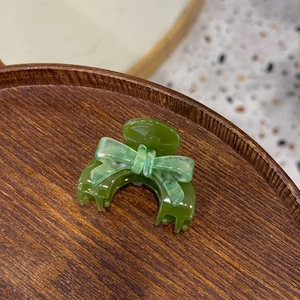 Detail of a dark green acetic hair claw with a light green translucent bow decoration