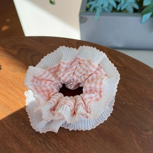 Pink and white striped chiffon scrunchie with wavy lace edges on a dark wooden background