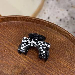 Detail of a black acetate hair claw clip with a stylish black and white checkered bow