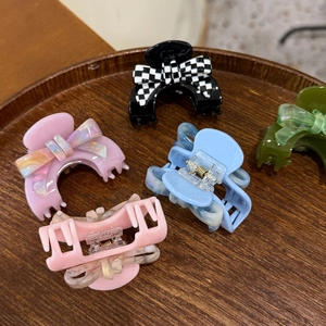 Close-up of five acetate hair claw clips in checkered bow and marble patterns on wood