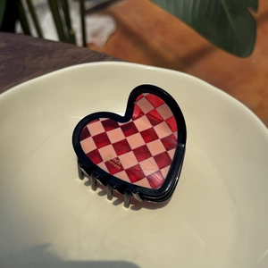 Pink checkered heart claw clip in acetate finish on a ceramic plate setting