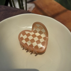 Detail of checkered heart-shaped acetate hair claw clip with golden handmade logo