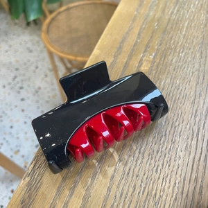 Detail shot of a two-tone hair claw clip with black shell and red transparent inner teeth