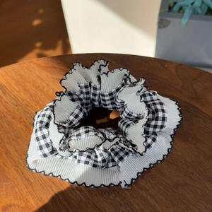 Detail of checkered and white knit scrunchie with black ruffled edges on wood