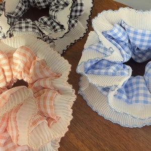 Detailed view of three checkered chiffon scrunchies with pleated ruffled edges on wood