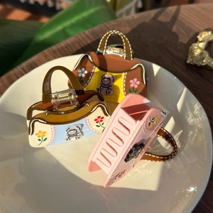 Detailed view of three bear and floral acetate hair claws in vintage handbag shapes