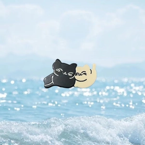 Détail de broches de chat en émail avec un chat noir et beige dans un câlin chaleureux