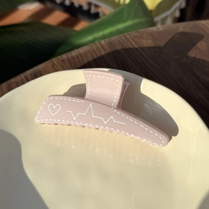 Pink heart-patterned plastic claw clip hair accessory in a ceramic plate on a wooden table