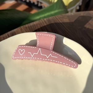 Detailed view of pink hair claw clip with heart and heartbeat pattern on a ceramic dish