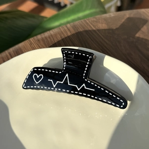 Detail of a black heart pattern hair claw clip on a stylish wooden table and ceramic plate