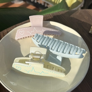 Three-piece pastel hair claw clips with heart pulse patterns on a ceramic plate