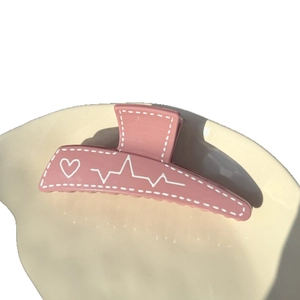 Pink heart pattern hair claw clip with white stitch design on a ceramic plate