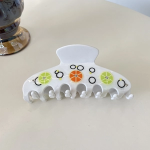 Détail d'une pince à cheveux en résine blanche avec imprimés citron, orange et strass