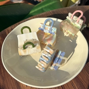 Detail view of acetate handbag-shaped hair clips with marble texture and pearl finish