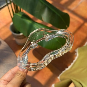 Close-up of a clear plastic cloud-shaped hair claw clip with a wave design in sunlight