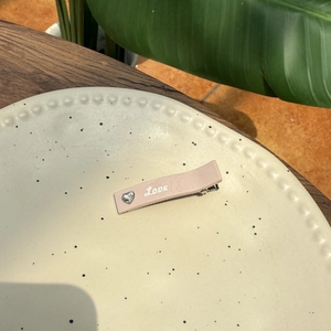 Gros plan d'une pince à cheveux rose avec texte Love et strass cœur sur un plat céramique