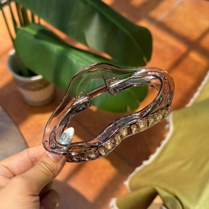 Handheld view of transparent amber cloud hair claw clip with wavy heart design