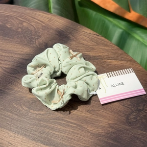 Green polka dot scrunchie with a gold bow tie and branding on a rustic wooden table