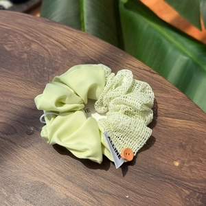 Detail of light green satin and mesh hair scrunchie with orange button on wood