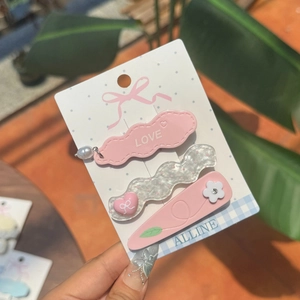 Set di tre fermagli per capelli dolci con perle rosa e incisione LOVE tenuti in mano