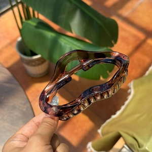 Detail view of a large brown tortoiseshell resin hair claw clip with wave edges and metal spring