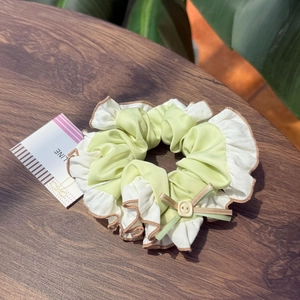 Detail of light green and white satin scrunchie with a small bow and cream button accent