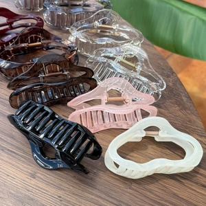 Macro detail of large wave-shaped plastic hair claws in various translucent colors on wood