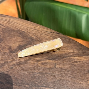 Fermaglio per capelli in acetato crema perlato con logo dorato su piano in legno