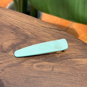 Dettaglio del fermaglio per capelli in acetato verde menta con logo dorato su legno