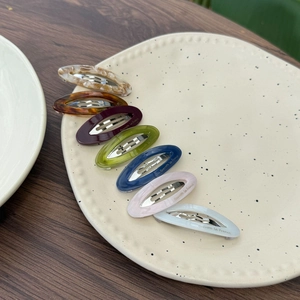 Detailed close-up of acetate water-drop hair clips with golden text on ceramic plate