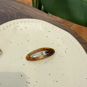 Detail view of acetate tortoise shell hair clip with gold text on a ceramic plate