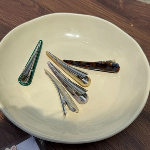 Detail of five colorful acetate horn hair clips arranged on a ceramic tray with wooden base