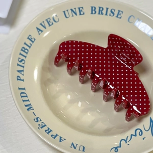 Close-up of a large red hair claw clip with white polka dots on a vintage ceramic plate