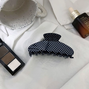 Close-up of a large black acetate hair claw clip with classic white polka dot patterns