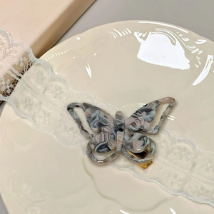 Macro view of butterfly hair clip showing marble texture and gold metal duckbill clamp
