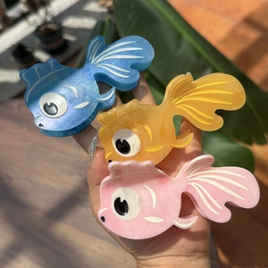 Détail de trois pinces à cheveux poisson en acétate bleues, oranges et roses