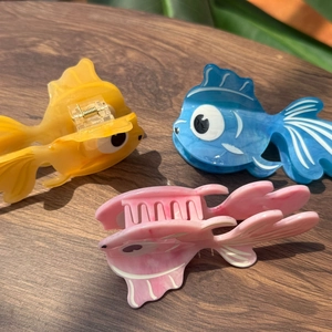Vue détaillée des pinces à cheveux poisson en acétate orange, bleu et rose sur bois