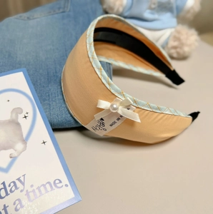 Detail of yellow fabric headband with silk bow, white pearl, and blue plaid edge trim