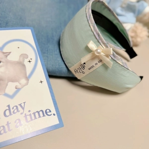 Detail of light green fabric headband with pearl bow and Korean love script label