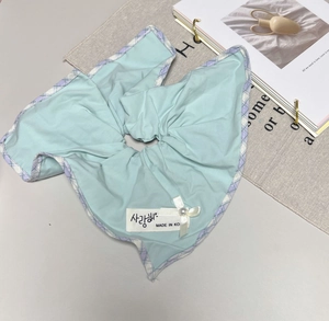 Detailed view of light blue hair scrunchie with purple check edge and pearl bow