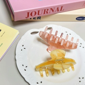 Elegant marble texture acetate hair claws in pink and yellow on a white ceramic plate