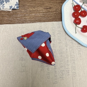 Detail view of denim and red polka dot pet bandana with cherry patch on linen background