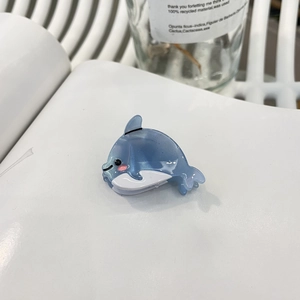 Gros plan d'une pince à cheveux dauphin en acétate bleu pailleté sur fond blanc épuré