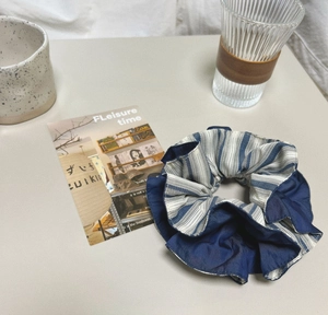 Detailed view of blue and white striped scrunchie with soft pleated cotton fabric texture