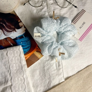 Détail d'un chouchou en maille bleu clair avec petits nœuds dorés et étiquette